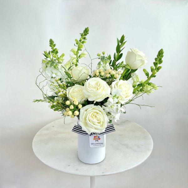 White roses and green-white blooms arranged in a white vase with a striped ribbon