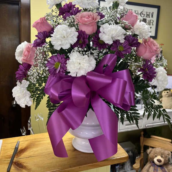 Pink roses and white carnations in a white vase with a purple ribbon