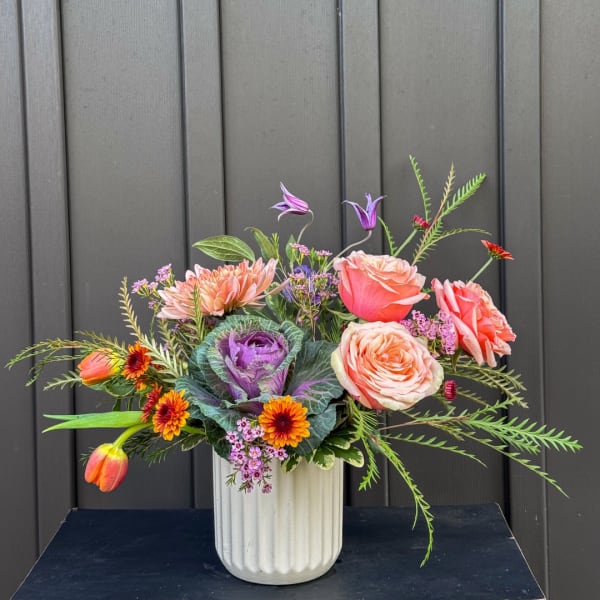 Mixed bouquet in a white ribbed vase with pink, peach, and purple blooms