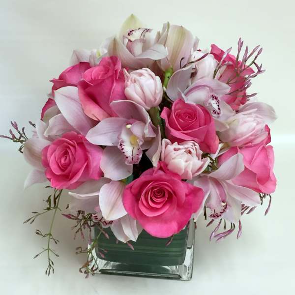 Pink roses and pale orchids arranged in a square glass vase