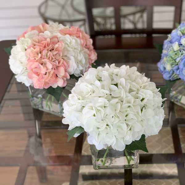 Three hydrangea arrangements in square glass vases on a table