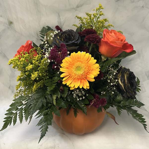 Autumn floral arrangement in a pumpkin-shaped container with roses and a yellow gerbera daisy