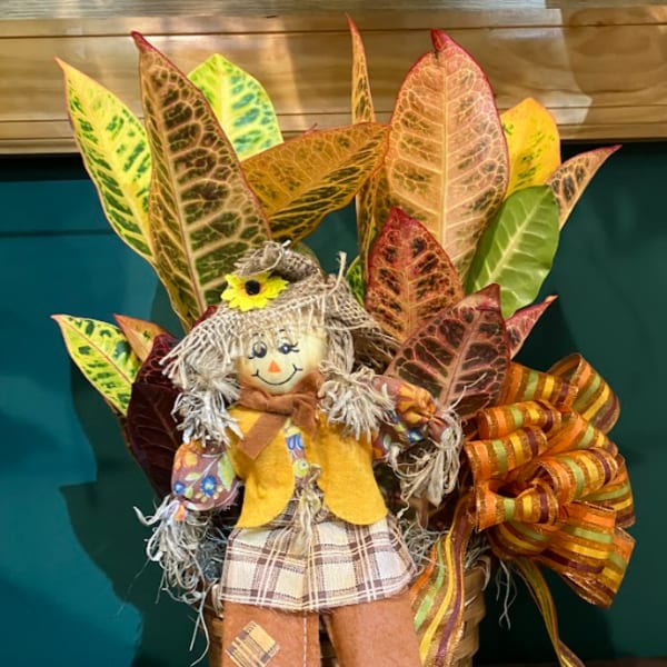 Fall scarecrow decoration in a basket with colorful leaves and ribbon
