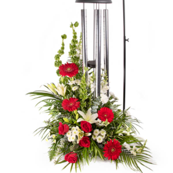 Standing floral arrangement with red gerberas, roses, and white lilies under a wind chime