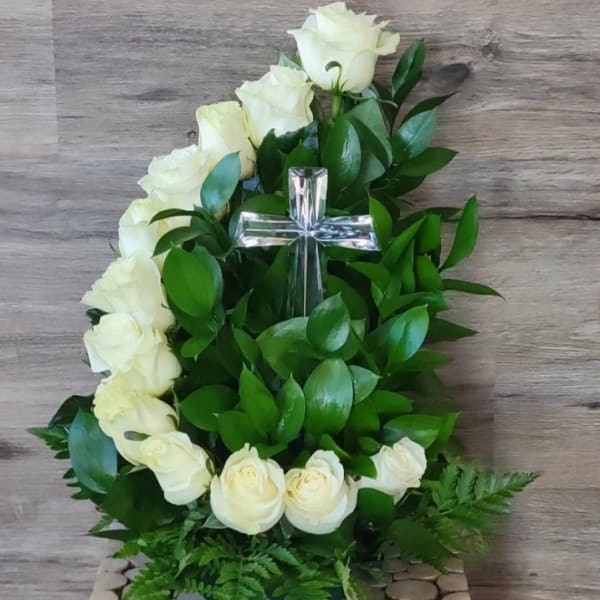 White roses arranged around a clear cross with green foliage