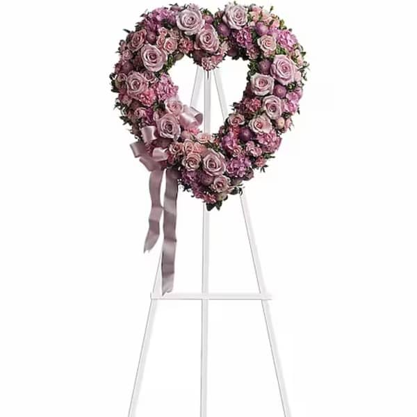 Heart-shaped pink rose wreath on a white stand with ribbon