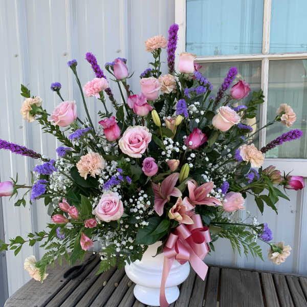 Pink and purple mixed flower arrangement in a white vase with a ribbon