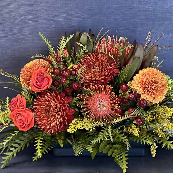 Low floral arrangement with orange and red blooms in a rectangular container