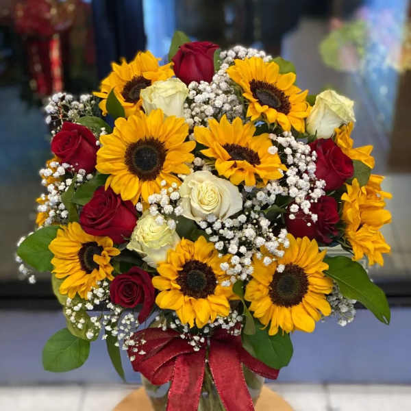 Bouquet of sunflowers and red and white roses in a glass vase with a red ribbon