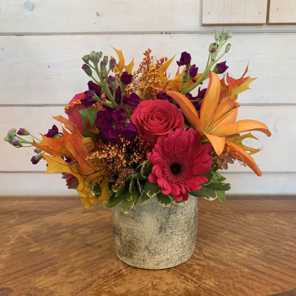 Bright mixed flower arrangement in a textured gray vase with orange leaves