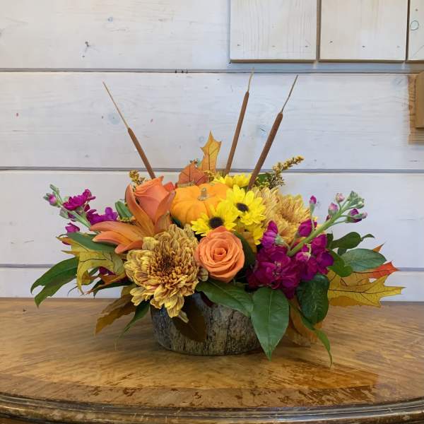 Autumn floral arrangement with sunflowers, roses, and a small pumpkin in a rustic container.