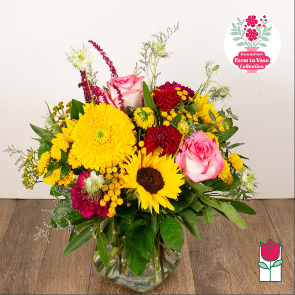 Mixed bouquet in a clear glass vase with pink roses, sunflowers, and yellow blooms
