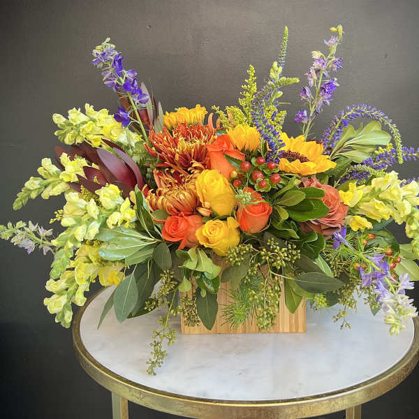 Colorful mixed flower arrangement in a wooden box on a round table