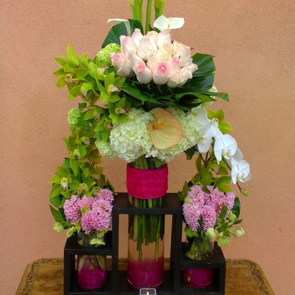 Tiered floral arrangement with white calla lilies, pink roses, and orchids in glass vases