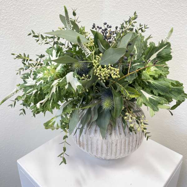 Green foliage arrangement in a ribbed white vase