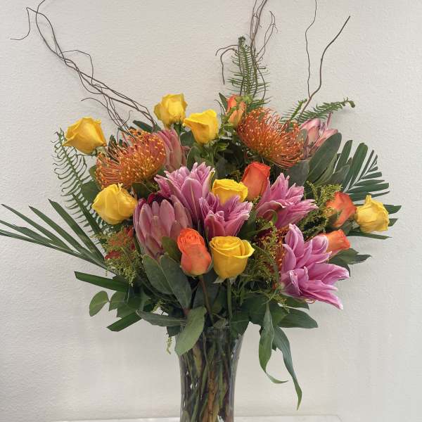 Tall mixed bouquet in a glass vase with yellow and orange roses and pink tropical blooms