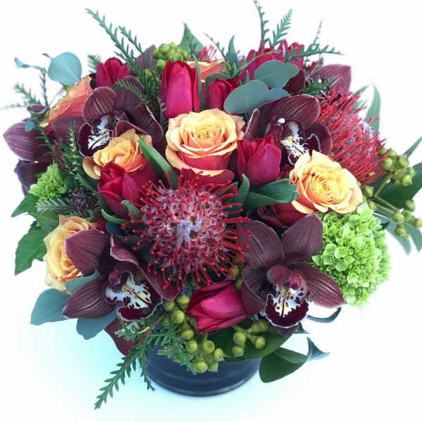 Bouquet of red tulips, peach roses, and dark orchids in a black vase