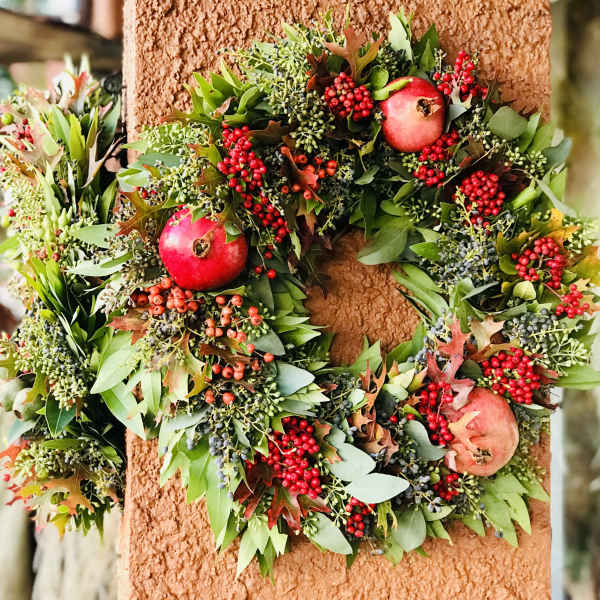 Autumn wreath with red berries and pomegranates on a textured wall
