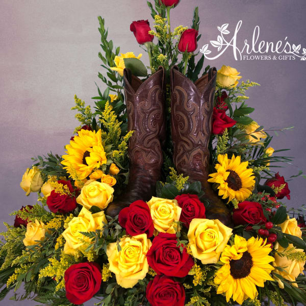Cowboy boots surrounded by red and yellow roses and sunflowers