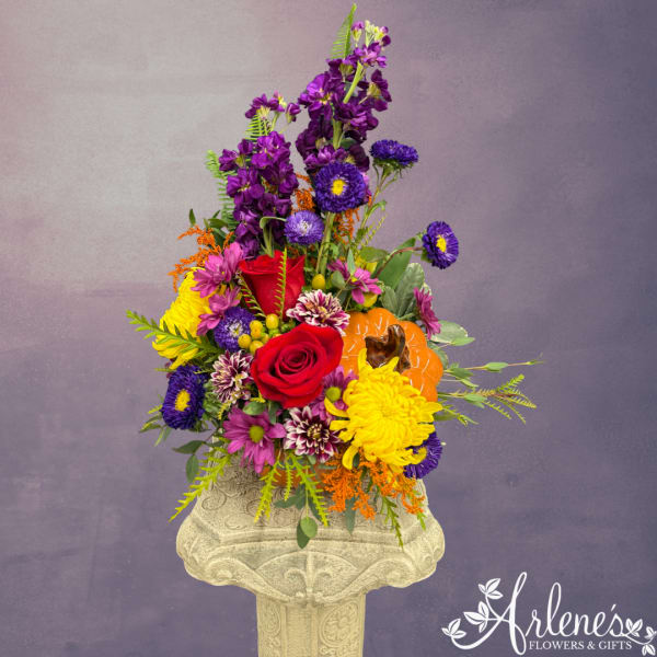 Colorful flower arrangement with roses, chrysanthemums, and a pumpkin accent in a pedestal vase