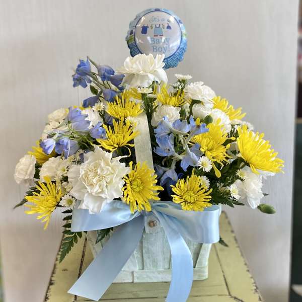 Blue and white flower arrangement in a basket with a baby boy balloon