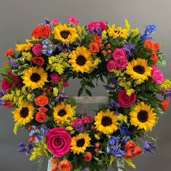 Heart-shaped floral wreath with sunflowers, roses, and blue accents on an easel