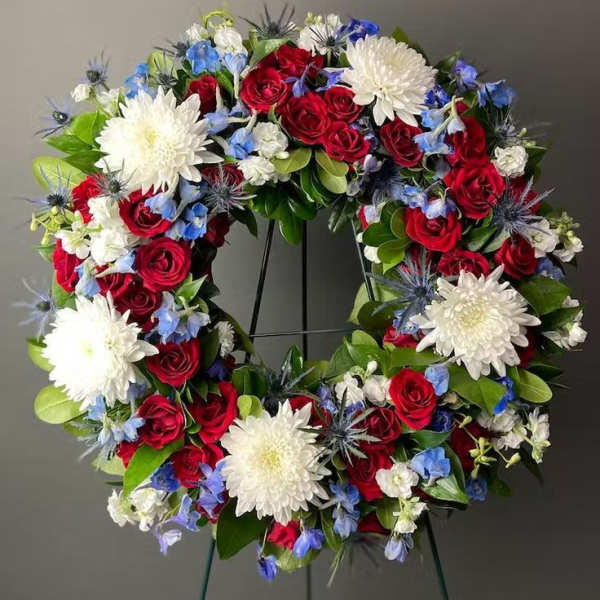 Circular wreath of red roses, white chrysanthemums, and blue flowers on a stand
