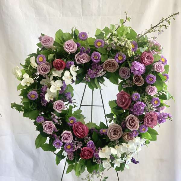 Heart-shaped floral wreath with pink and purple flowers on a metal stand