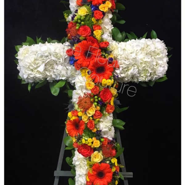 Floral cross arrangement with white blooms and bright mixed flowers on an easel