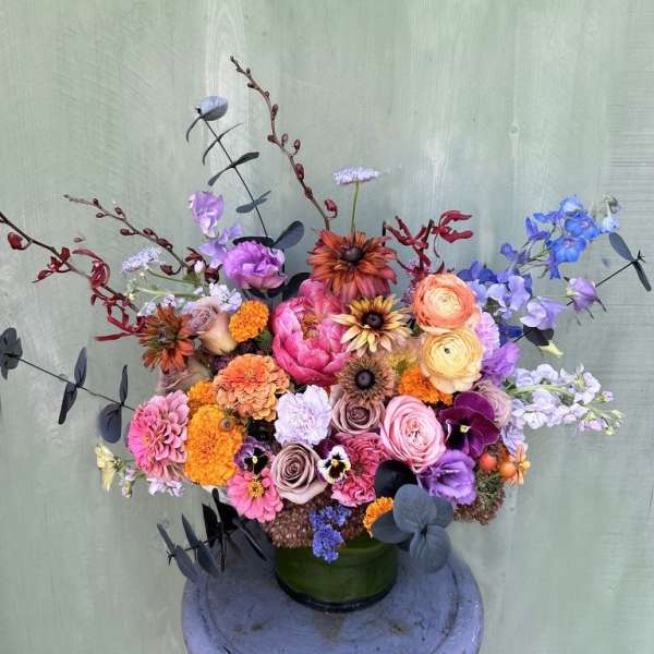 Colorful mixed bouquet in a green vase with pink, orange, purple, and blue blooms