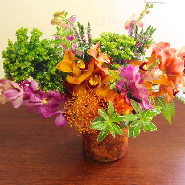 Mixed orchid arrangement in a brown vase with orange and purple blooms