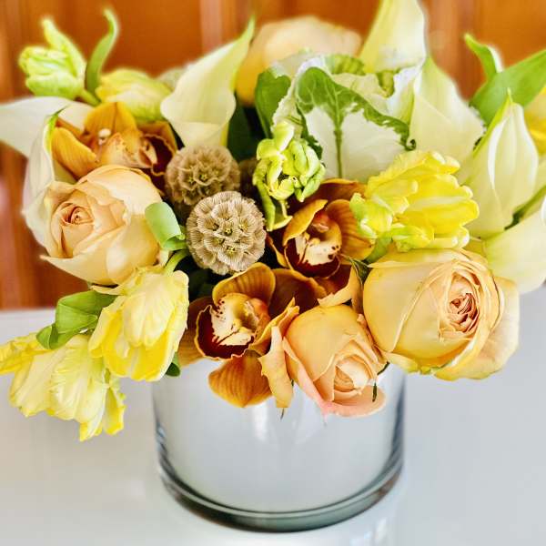 Bouquet of peach roses, yellow blooms, and white flowers in a glass vase