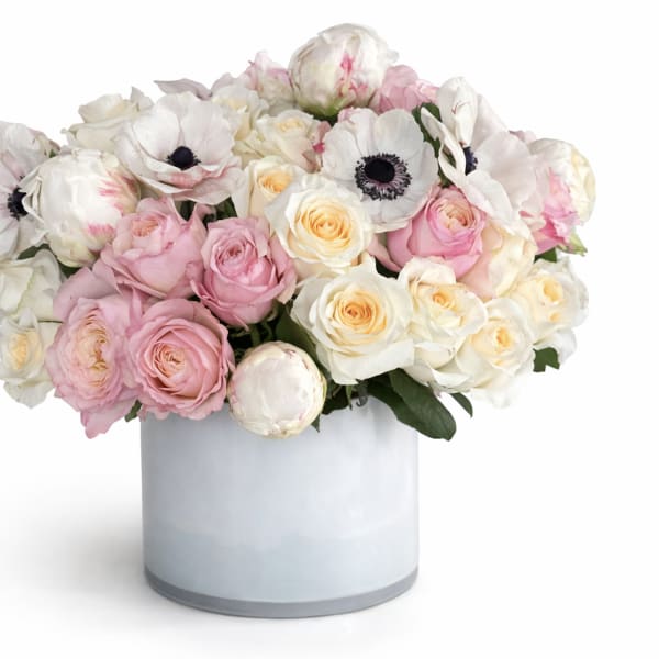 Low pastel arrangement of pink and cream roses with white anemones in a white cylinder vase