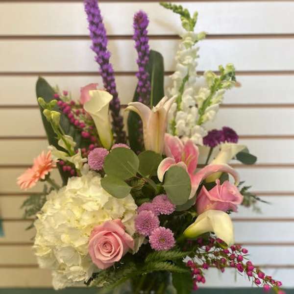 Mixed bouquet with pink roses, white hydrangea, and calla lilies in a glass vase