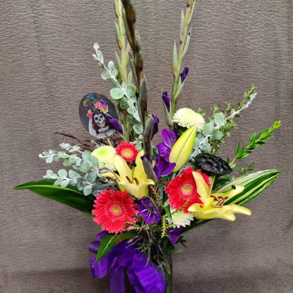 Tall floral arrangement with lilies, gerbera daisies, and purple ribbon
