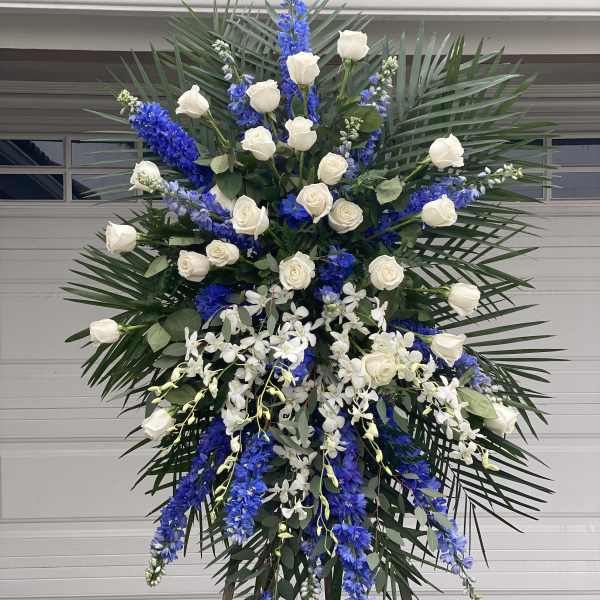 Tall standing floral spray with white roses, blue delphinium, and white orchids