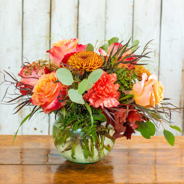 Mixed bouquet of orange, pink, and yellow flowers in a glass vase