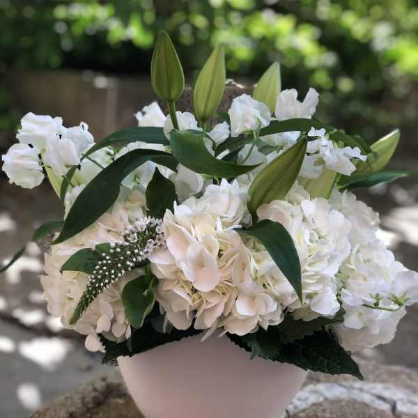 White floral arrangement with lilies and hydrangeas in a pale vase