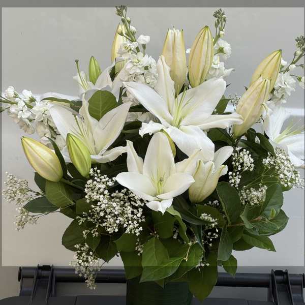 White lilies and buds arranged in a green vase with baby's breath