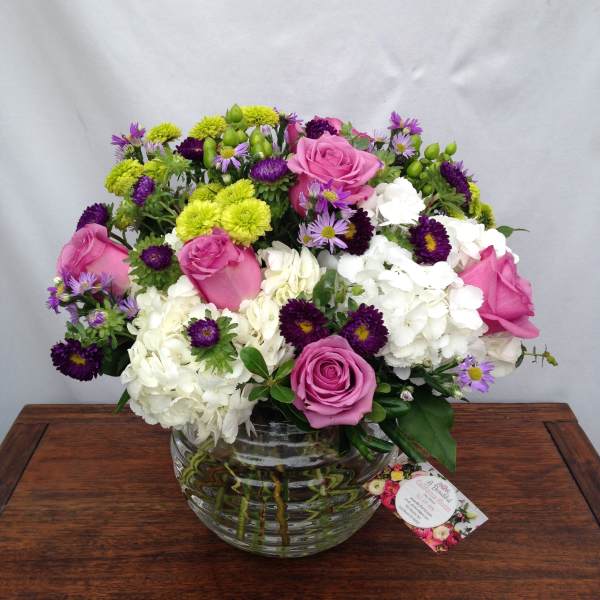 Pink roses and white hydrangeas in a clear glass vase with purple and green accents