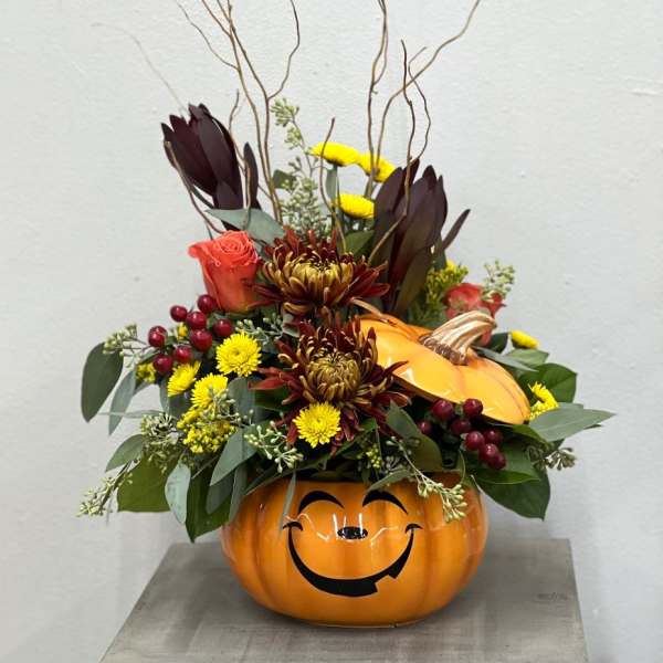 Fall floral arrangement in a smiling pumpkin container with mixed blooms