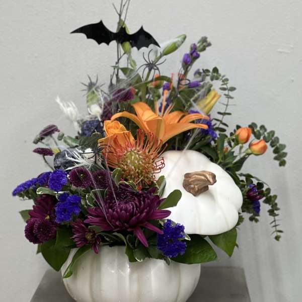Halloween floral arrangement in a white pumpkin container with a bat topper