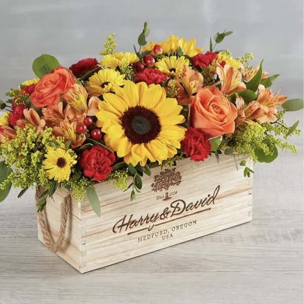 Mixed flower arrangement in a wooden crate with sunflowers and roses