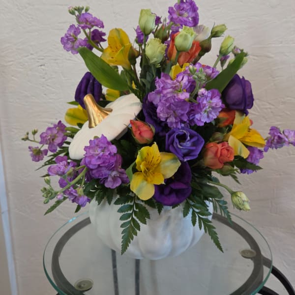 Purple and yellow floral arrangement in a white pumpkin-shaped container