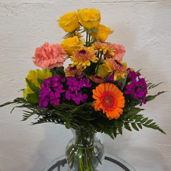 Colorful mixed bouquet in a clear glass vase with roses, gerberas, and carnations