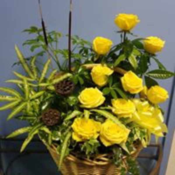 Yellow roses arranged in a woven basket with spiky green foliage