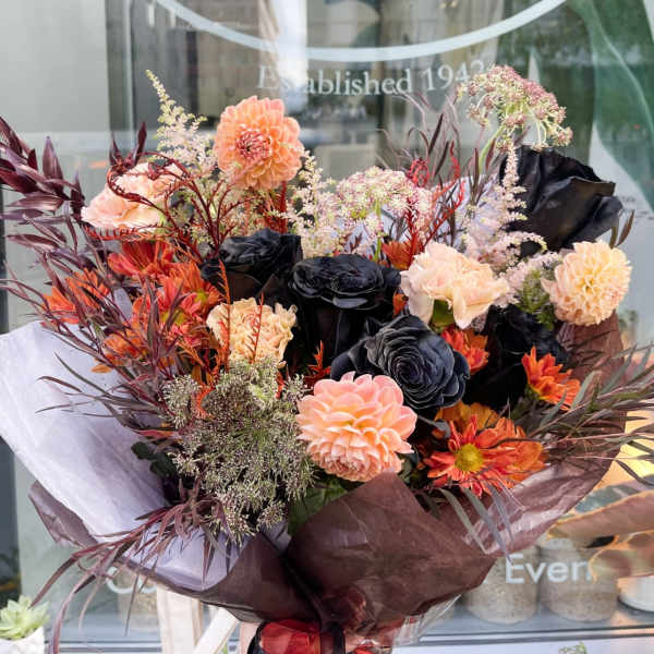 Bouquet of peach, orange, and black flowers wrapped in dark paper