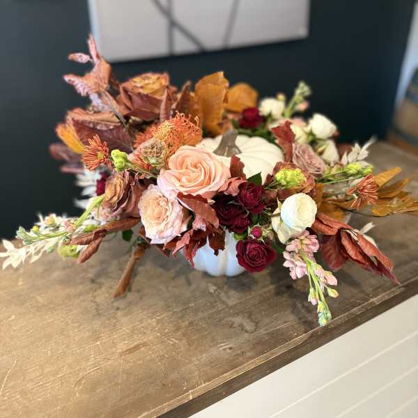 Low floral centerpiece in a white pumpkin container with roses and autumn leaves