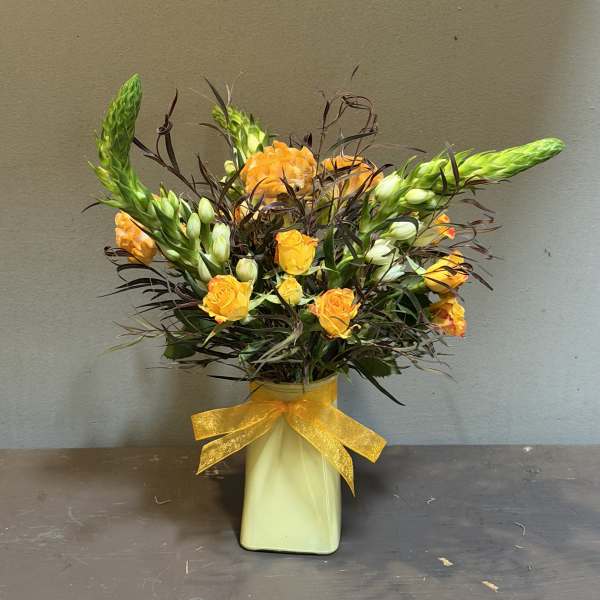 Orange roses in a pale vase with a yellow ribbon