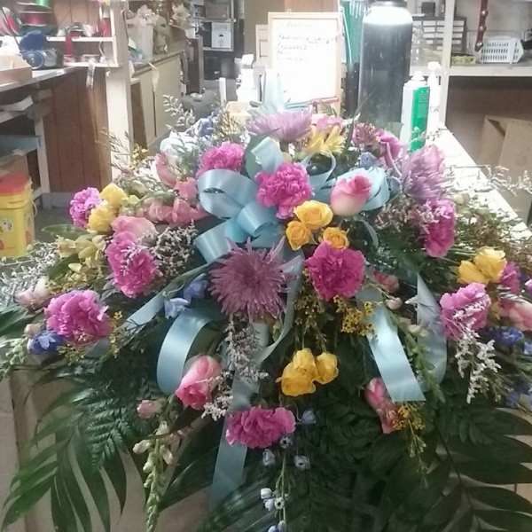 Large colorful funeral spray with pink, yellow, and blue flowers